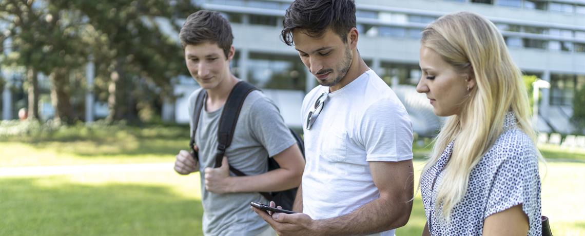 Studierende laufen über den THU-Campus und schauen auf ein Handy. 