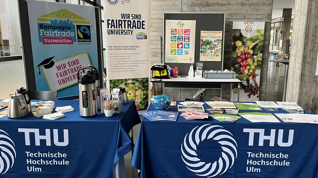 Tisch mit Flyern und fairen Getraenken mit einem Fairtrade Plakat im Hintergrund