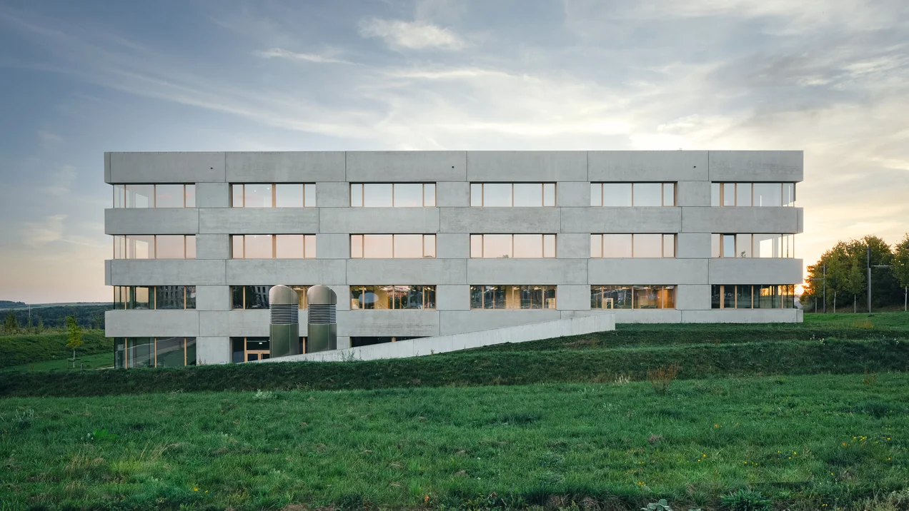 Wide-angle shot of a modern, square new building with a green meadow in front of it.