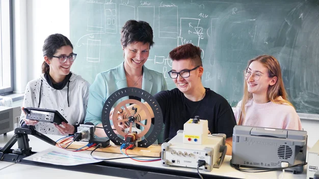Das Bild zeigt eine Professorin mit Studentinnen im Hörsaal.