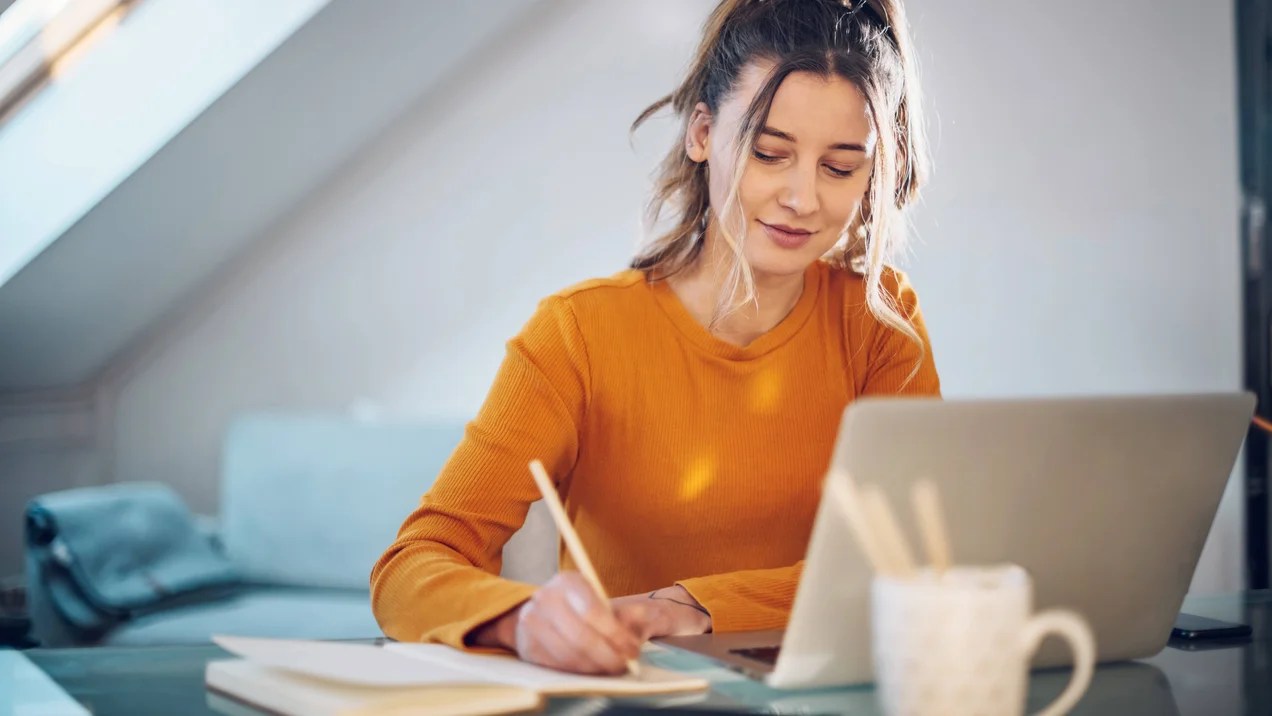 Person ist zu Hause und macht Arbeit an ihrem Laptop und schreibt etwas auf