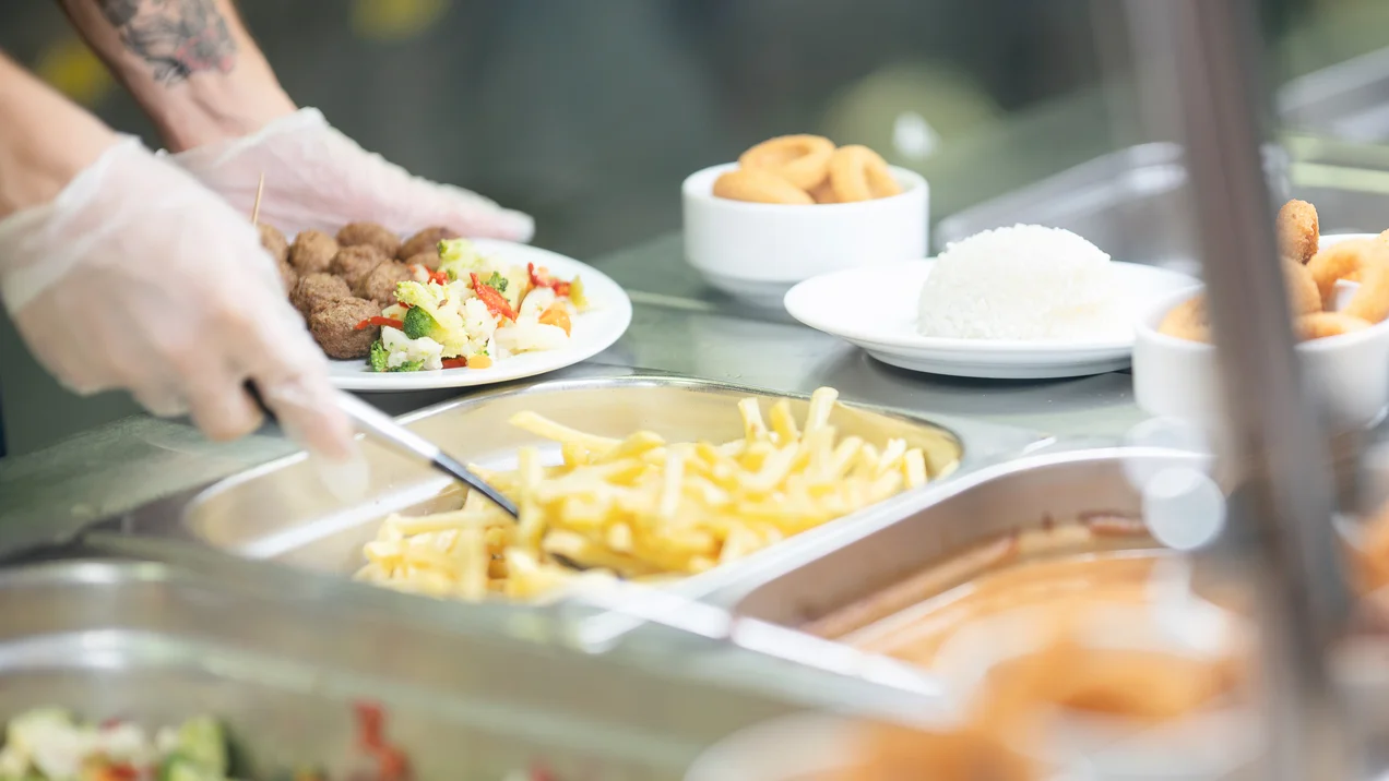 Eine Mensa Mitarbeiterin bereitet ein Mittagessen zu.