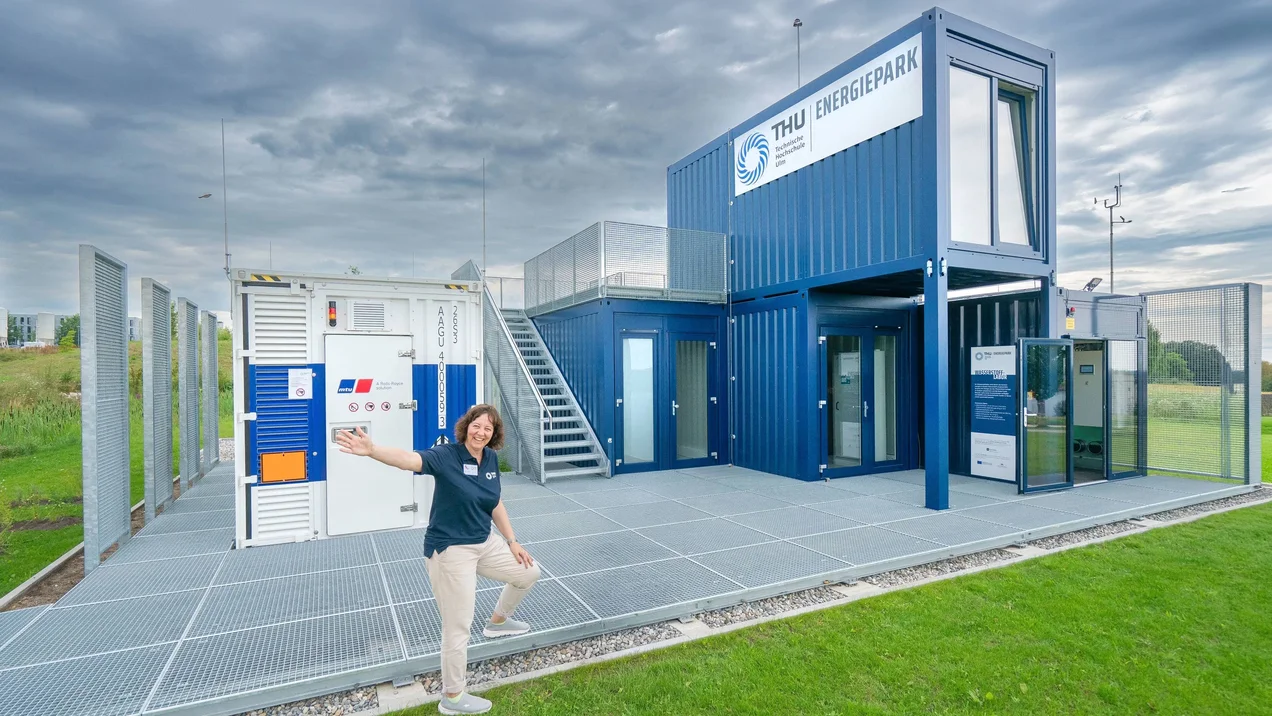 Mitarbeiterin präsentiert den THU Energiepark, einen blauen Containerbau.