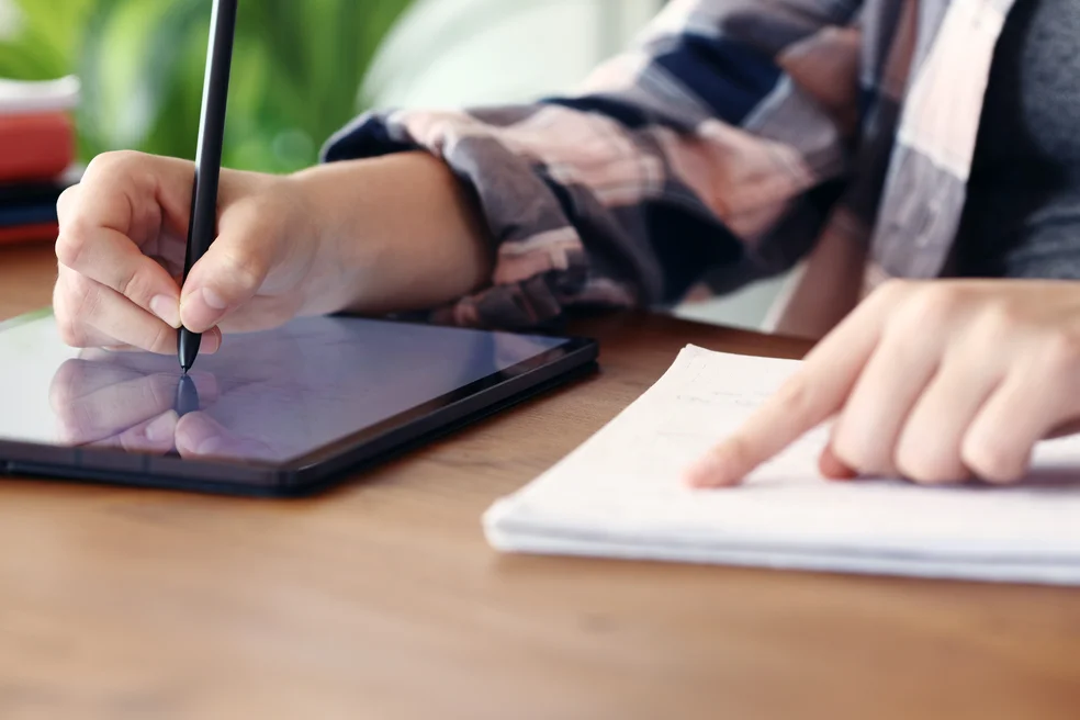 Student hands writing on tablet checking paper notebook