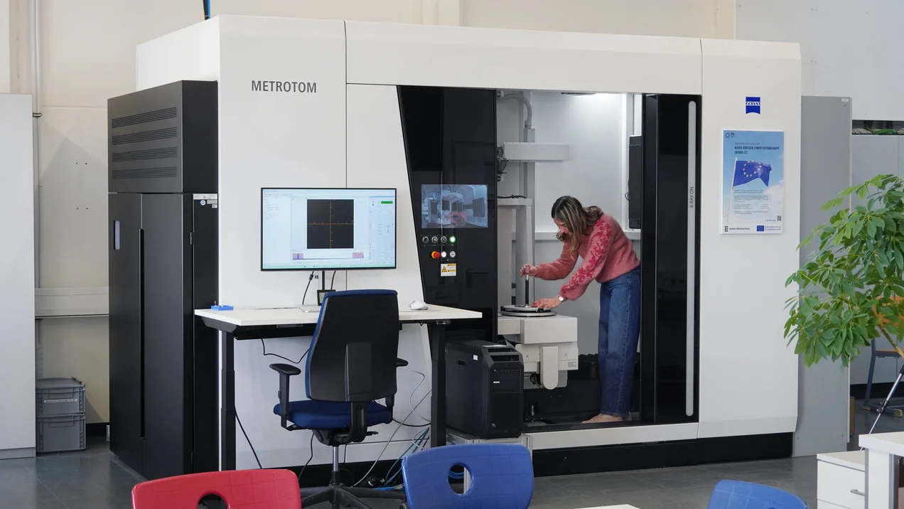 Person steht im Computertomograph und platziert eine Probe.