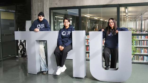 Drei junge Erwachsene sitzen auf den THU Buchstaben zu einem Gruppenbild