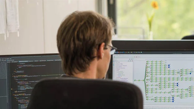Person arbeitet an Programmcode und der Visualisierung eines KI-Systems auf mehreren Bildschirmen.