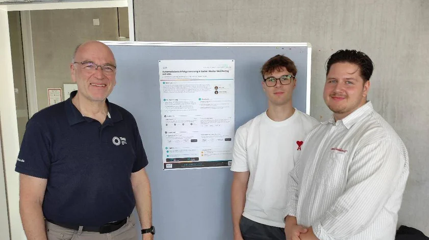 After presenting their practical project for the Business Informatics program, two students and a professor are standing together in an office in front of a presentation poster.