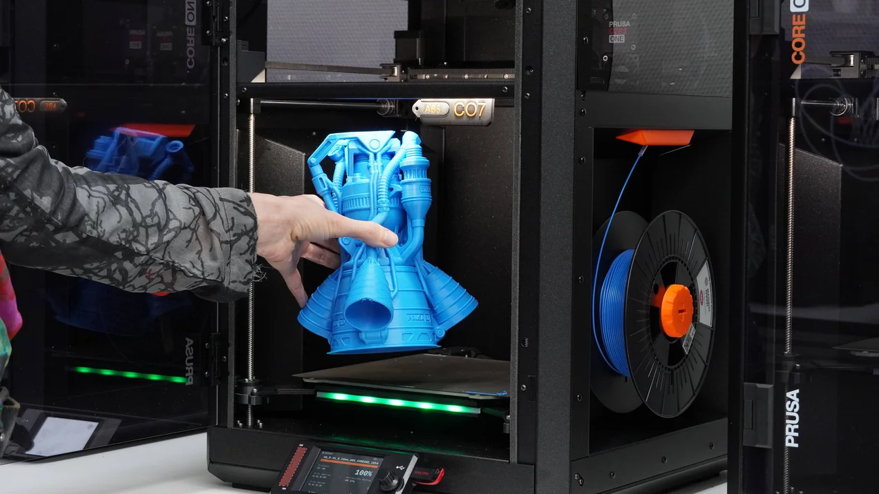 Eine Person holt eine gedruckte, blaue Turbine aus einem 3D-Drucker