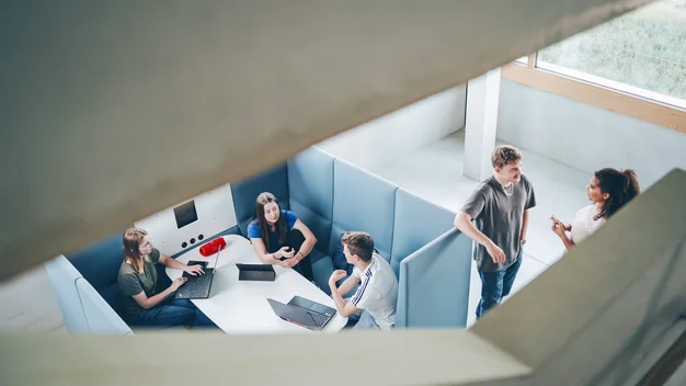 Vogelperspektive in einem modernen, offenen Gebäude: Personen bei der Gruppenarbeit in einem hellen Atrium. Stark für Architektur- und Community-Themen.