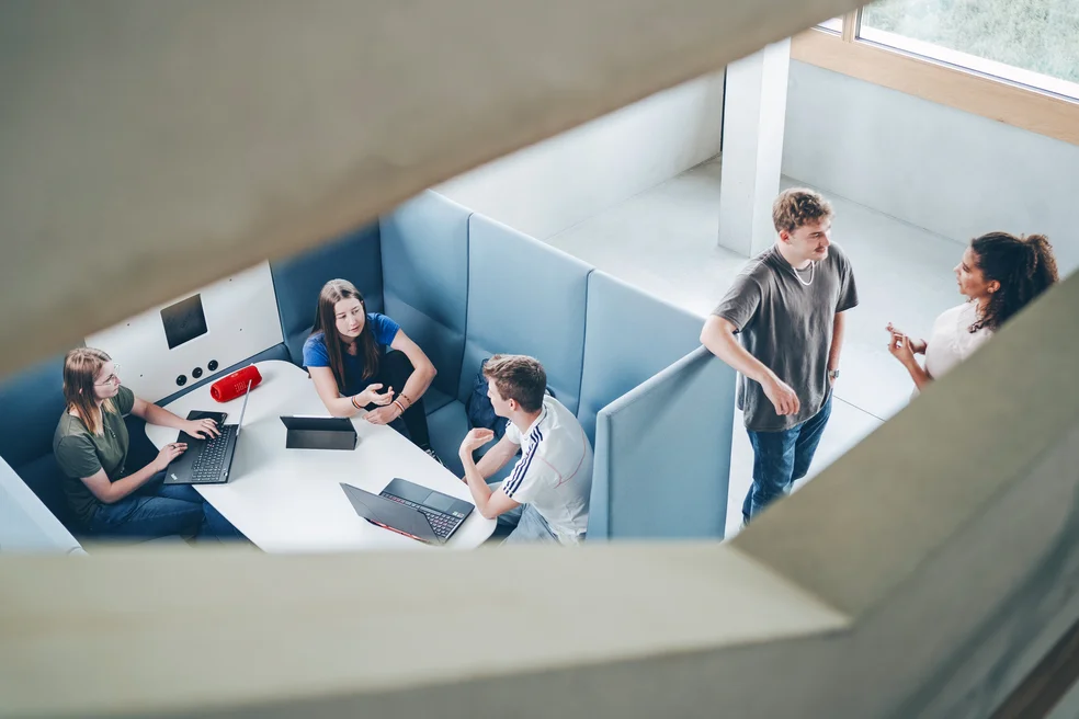 Vogelperspektive in einem modernen, offenen Gebäude: Personen bei der Gruppenarbeit in einem hellen Atrium. Stark für Architektur- und Community-Themen.