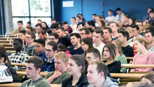 Dicht sitzende Studierende in einem Hörsaal, der Fokus liegt auf den Zuhörern.