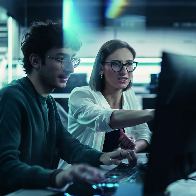 Zwei junge Ingenieure die am Computer arbeiten und sich am Arbeitsplatz unterhalten. Weibliche und männliche Softwareentwickler diskutieren eine Lösung für ihr kollaboratives Projekt zur künstlichen Intelligenz