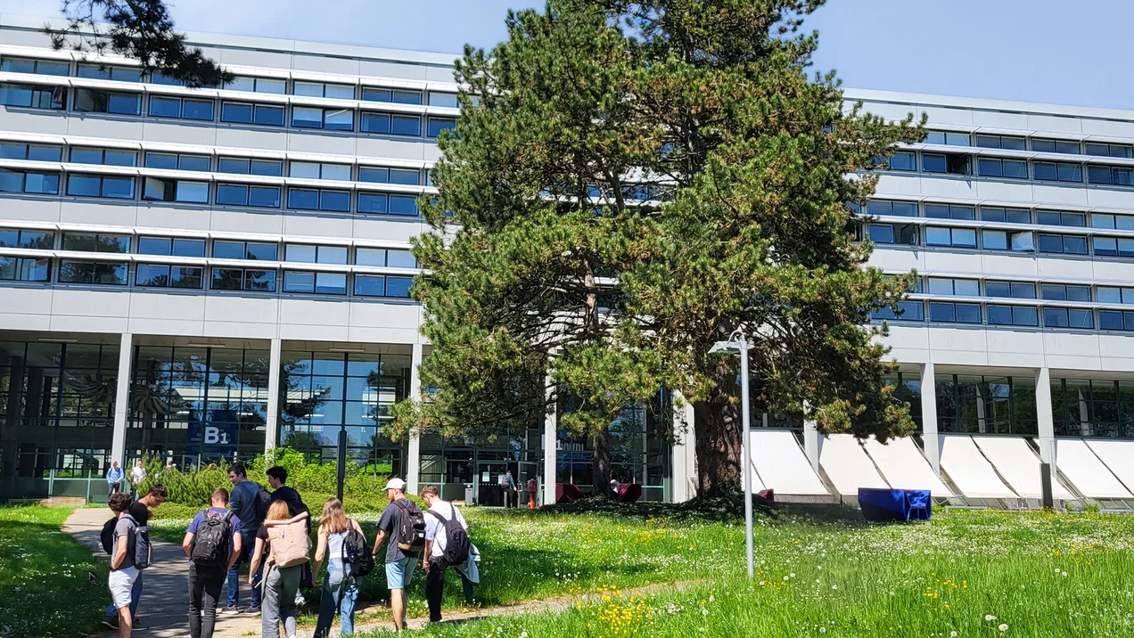 Gruppe von Studierenden geht auf den modernen Glaseingang des Hauptgebäudes der TH Ulm am Campus Prittwitzstraße zu.