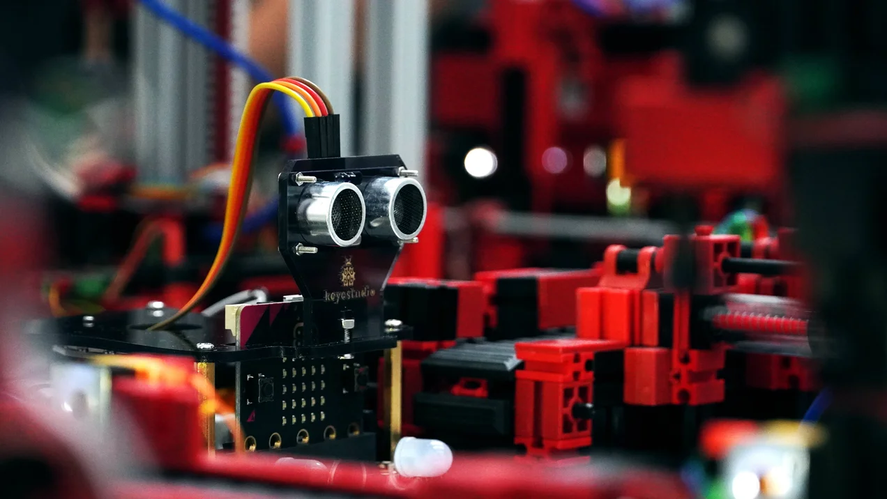 Nahaufnahme von technischen Einzelteilen eines Forschungsaufbaus zur Industrie 4.0 in Fischertechnik. Aus mehreren Einzelteilen verlaufen Kabel.