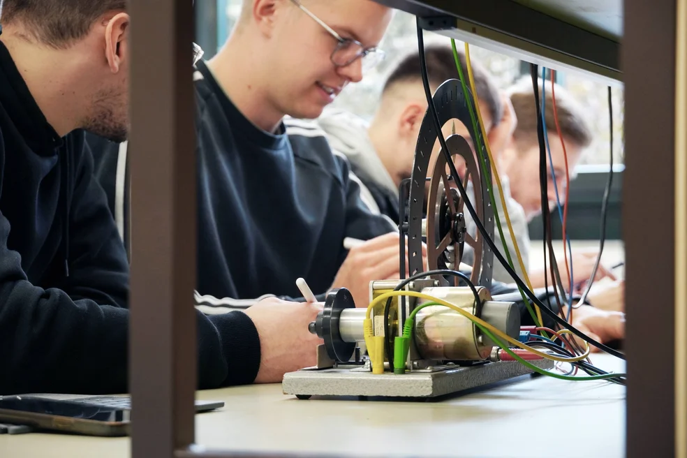 Studierende sitzen hinter einem Rad beim Versuch im Physiklabor