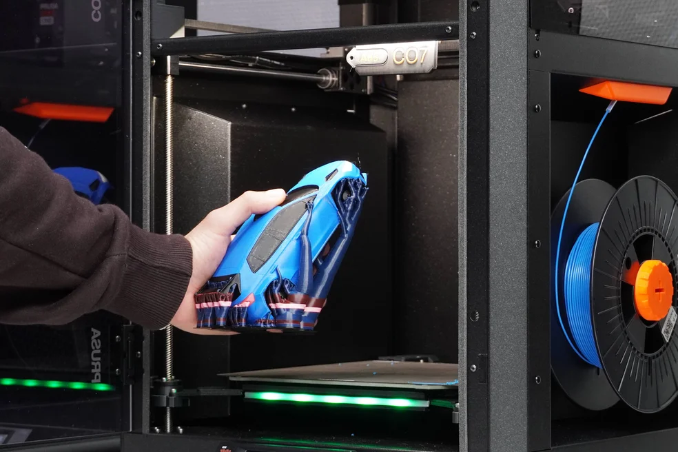 Jemand holt ein gedrucktes, blaues Auto aus einem 3D-Drucker