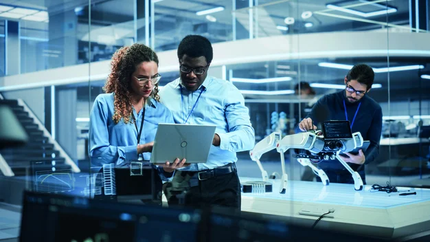 Porträt von zwei multiethnischen Ingenieurinnen und Ingenieuren Verwenden Sie einen Laptop-Computer, um sich zu verbinden, zu analysieren und zu diskutieren, wie man einen Roboterhund programmiert. Stehen im High-Tech-Forschungslabor mit moderner Ausstattung